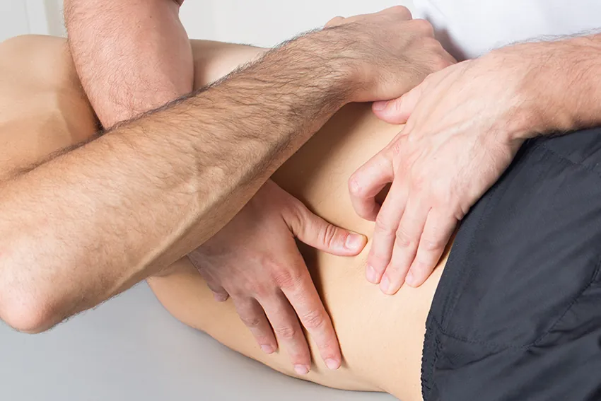 Rolfing-Behandlung: Therapeut löst mit beiden Händen Faszienspannungen im Bereich von Hüfte und Rumpf